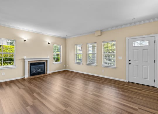 Little Tuscany Apartments & Townhomes - Living Room showing fireplace, multiple windows and front door. Vinyl plank wood flooring, white woodwork