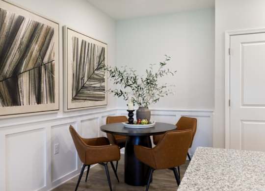A dining room with a table, chairs, and two paintings on the wall.