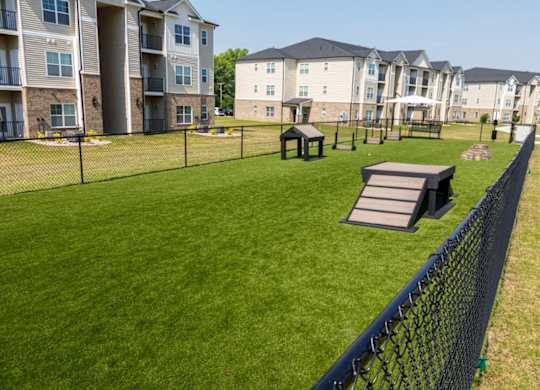A grassy area with picnic tables and a fence in front of apartment buildings.