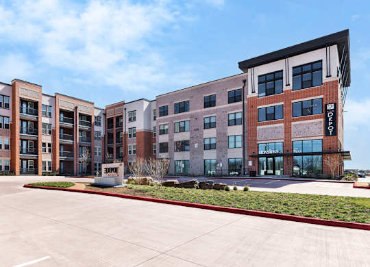 A row of modern apartment buildings with a parking lot in front.