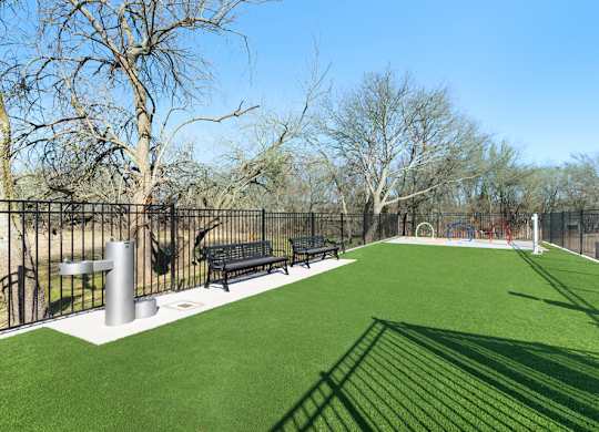 A park with a green field and a black fence.