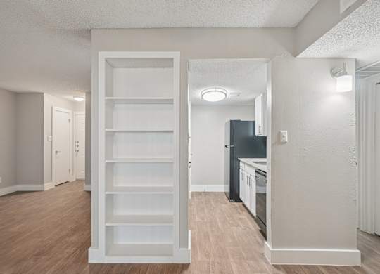 A white shelving unit in a room with a kitchen in the background.