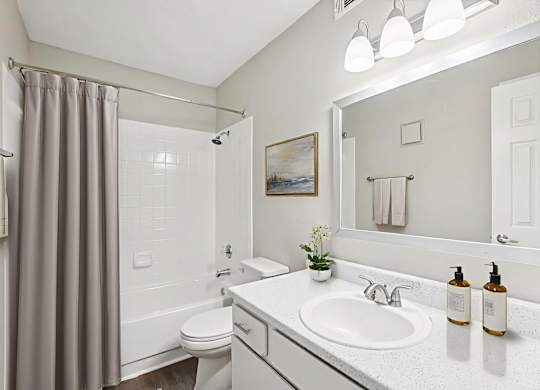 A bathroom with a white sink, toilet, and a grey shower curtain.
