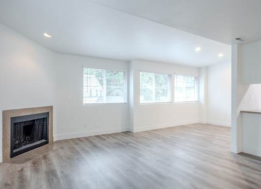 Spacious living room with wooden style flooring, large windows, and a fireplace at The Rosewood Apartments in Vancouver, Washington.