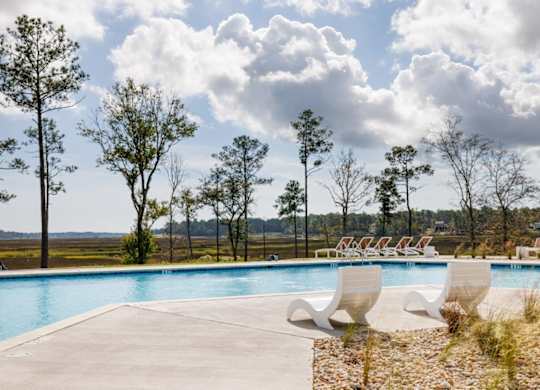 A pool surrounded by trees and chairs.