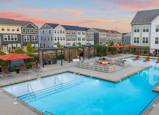 A large swimming pool surrounded by a deck with chairs and umbrellas.
