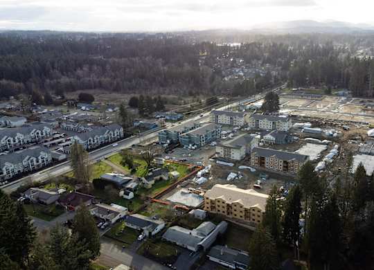 Aerial view of The Elowen apartment construction in Lacey WA amid towering evergreen trees on an overcast Pacific Northwest day.