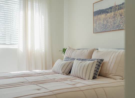 A bed with a white comforter and striped pillows with a plant on it.