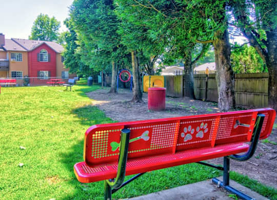 A red bench with a dog paw print design sits in a grassy area.