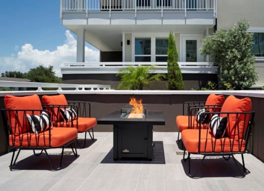 a fire pit on a patio with orange chairs and a black table