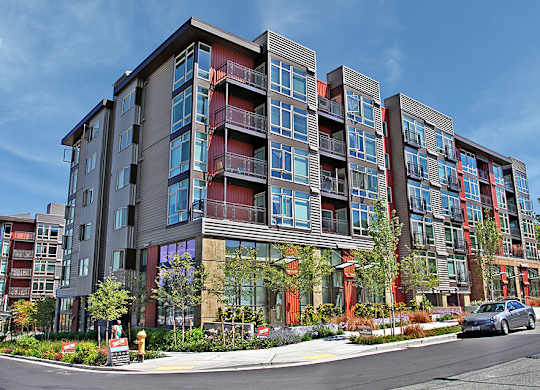 A modern apartment building with balconies and trees in front.