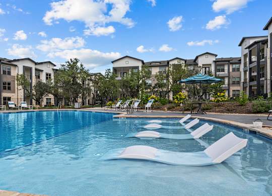 A swimming pool with lounge chairs and apartment buildings in the background.