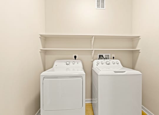 In-unit white washer and dryer set with shelving above and white walls at Sylvan Uptown,Colorado, Denver