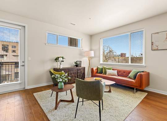 Spacious living room with a couch and chairs surrounding in natural light from the windows and door leading out to the balcony at Sylvan Uptown, Colorado