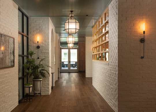 Long white brick hallway with wood flooring and geometric pendant lighting leading to resident lounge at Sylvan Uptown, Colorado