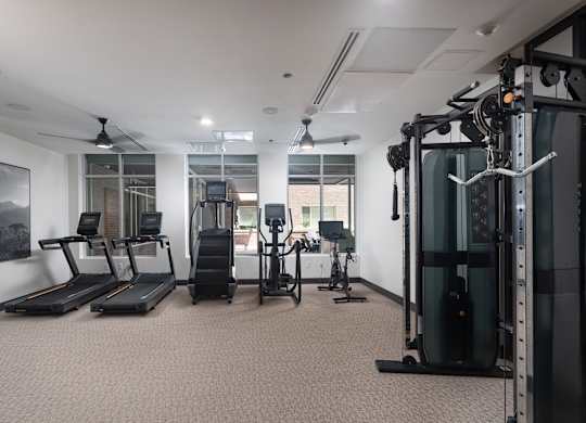 Resident gym with two treadmills, a stairstepper, an elipitcal, and a stationary bike with a television facing the large windows weights and mirrors in a room with a window at Sylvan Uptown, Denver
