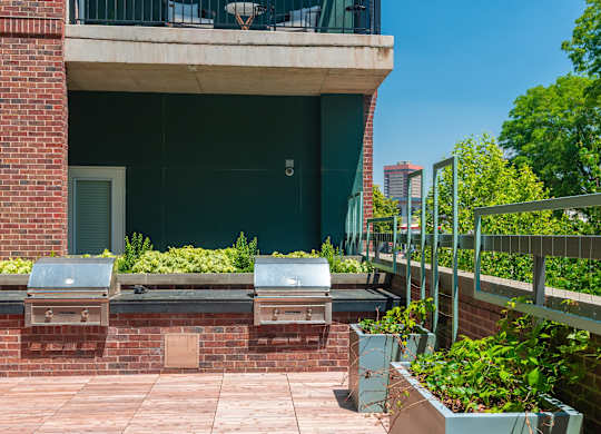 Red brick patio lounge with plants and two BBQ grills at Sylvan Uptown, Denver