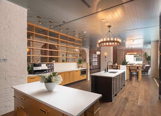 View into the luxurious resident demo kitchen and lounge spaces and dining area of a modern home with wood floors and white countertops at Sylvan Uptown, Colorado, Denver