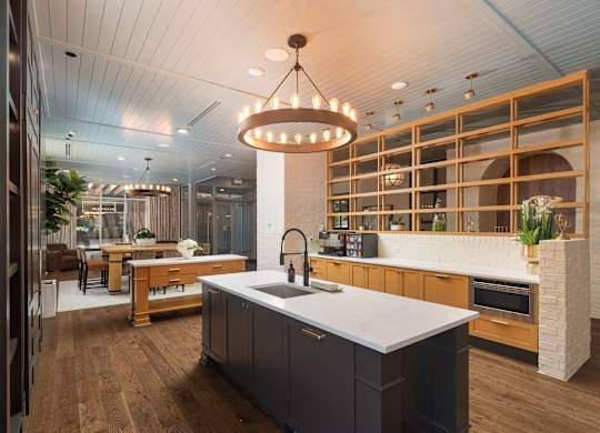 Gorgeous resident kitchen and lounge area with a patterned wood and brick half-wall, dark island cabinetry with gold hardware and sink, and view into the chic seating area at Sylvan Uptown, Denver, CO