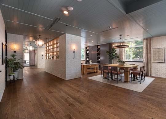 View of the resident lounge with white brick walls, square wooden table with cognac colored chairs and wooden floors  at Sylvan Uptown, Denver