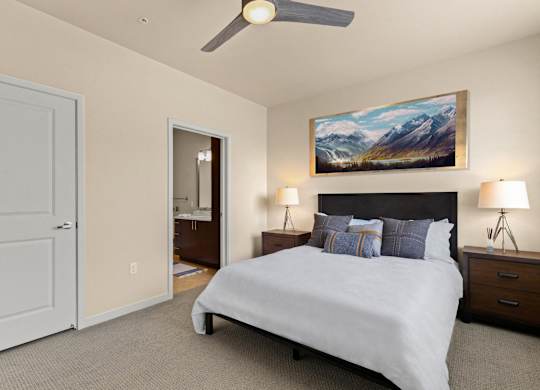View into the cozy bedroom with a large bed, two side tables, and a ceiling fan with access into the bathroom at Sylvan Uptown, Denver