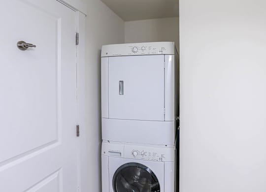 A white dryer and washer are stacked on top of each other in a small room at Park87 Apartments, Massachusetts