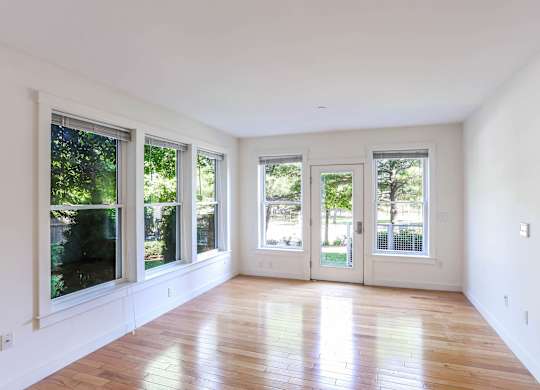 A room with white walls and wooden flooring, with three windows and a door at Park87 Apartments, Cambridge, MA, 02138