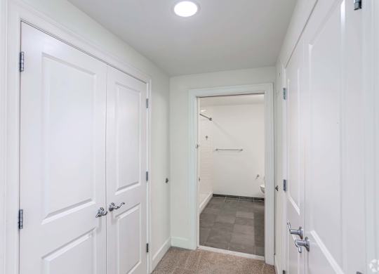 A white hallway with a door on the left and a bathroom on the right with plenty of storage at 7 Cameron Apartments, Massachusetts, 02140