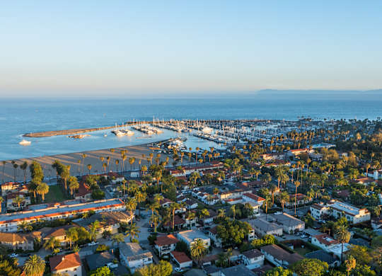 A coastal town with a pier and boats is seen from above.