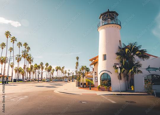 A white lighthouse with a black top stands in front of a building with a sign that reads