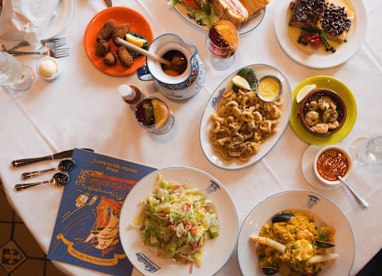 A table with a white tablecloth is set with plates of food, glasses, and a menu.