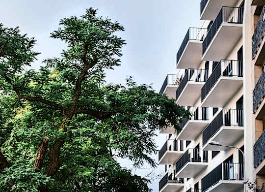 A tall building with balconies is surrounded by trees.