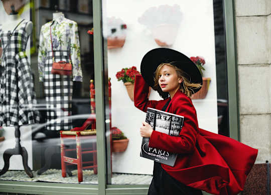 a woman in a red dress holding a magazine standing in front of a store window