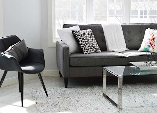 A black chair sits next to a grey couch with a glass table in between.