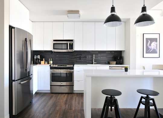 A modern kitchen with a refrigerator, microwave, oven, and bar stools.
