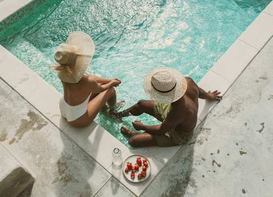 Two people sitting by a pool with a plate of food in front of them.