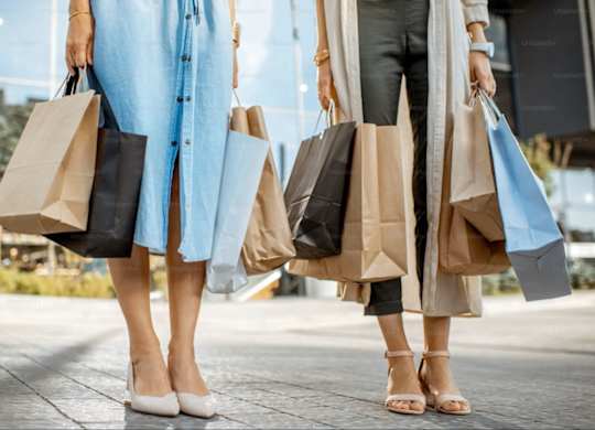 Two women carrying shopping bags walking on a sidewalk.