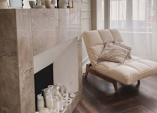 A white chair with a cushion is placed in front of a marble fireplace.