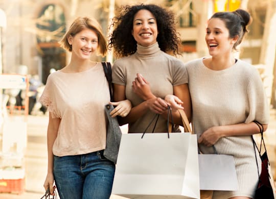 Three women are walking down the street carrying shopping bags.