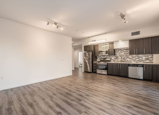 an empty living room and kitchen with wood flooring and a stainless steel refrigerator