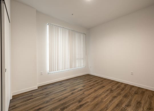 a bedroom with white walls and wood flooring and a window