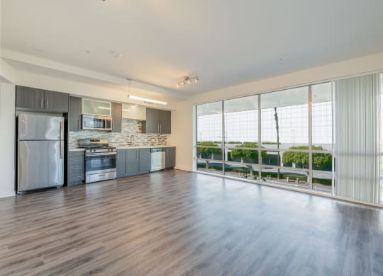 an empty living room with a kitchen and a large window