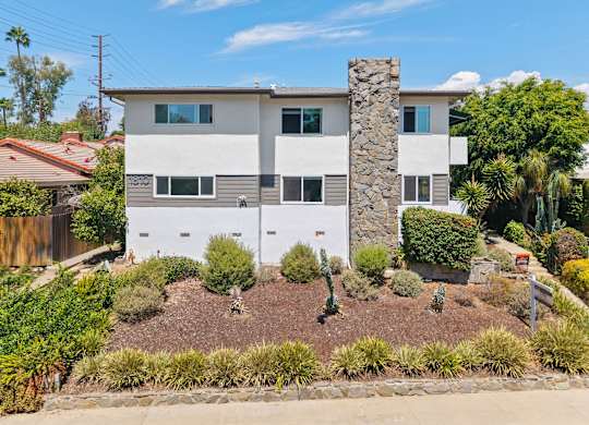 A house with a white and grey exterior and a stone pillar in the front yard.