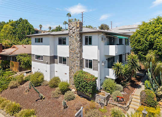 A white two-story house with a stone chimney and a garden in front.