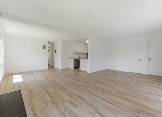 A spacious room with wooden flooring and white walls.