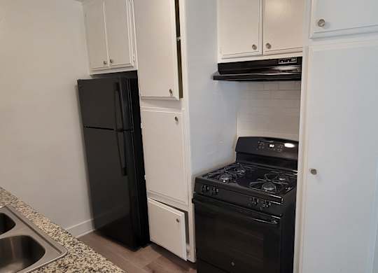 A black refrigerator is in a kitchen with white cabinets.