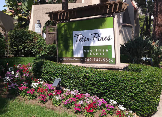 Enterance monument sign surrounded by beautiful gardens at Teton Pines Apartments in Escondido, California.