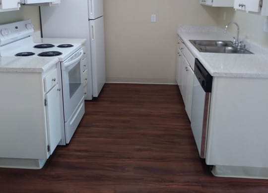 Kitchen with dark hardwood flooring and white kitchen appliances and cabinets at Teton Pines Apartments in Escondido, California.
