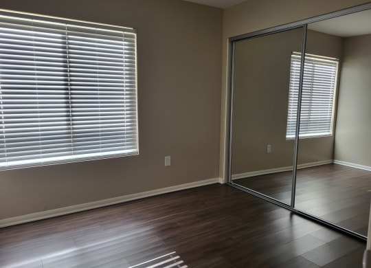 Bedroom with plank style flooring, large window and large closet with sliding mirror doors at The Cove at Bear Valley in Escondido, California.
