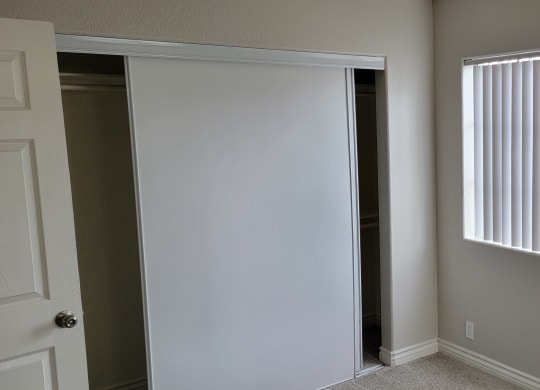 Carpeted bedroom with large closet and window at Lakeshore Terrace Apartments in Lakeside, California.
